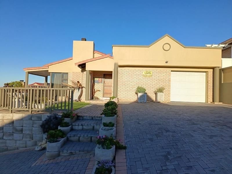 Front elevation of a single-story house featuring a paved driveway, single garage, brick facade, and a raised deck area with retaining wall.
