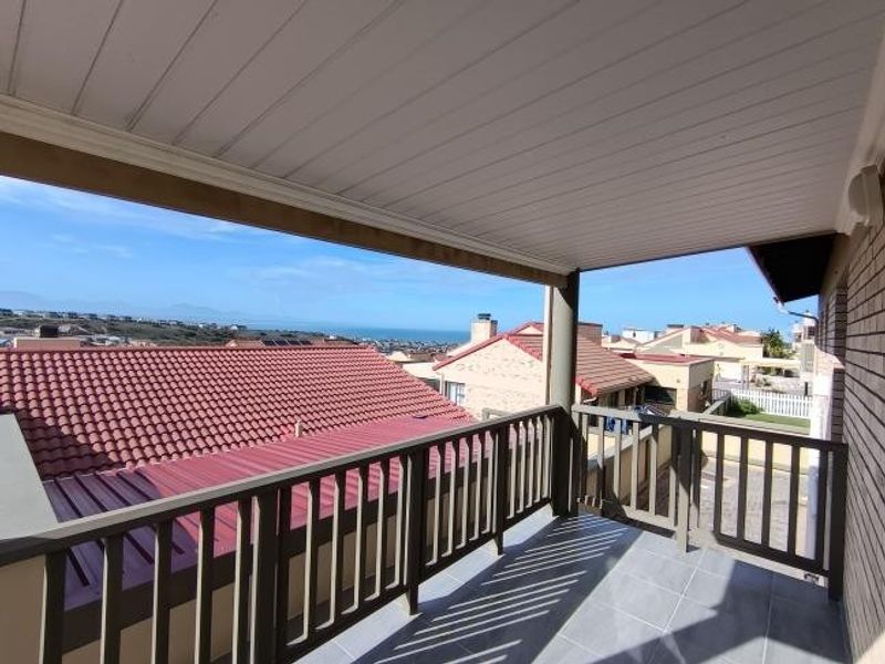 A covered balcony featuring tiled flooring and a railing, offering elevated views of the surrounding neighborhood and distant ocean.