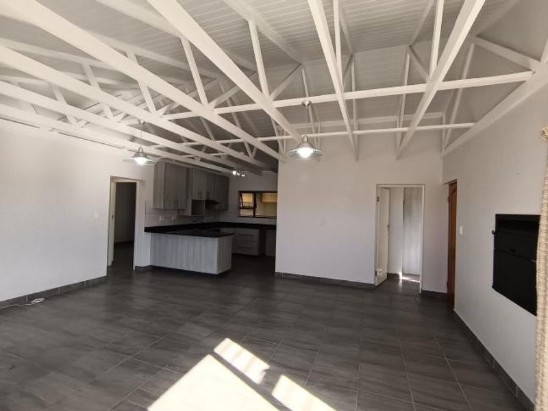 Spacious open-plan living area featuring high exposed truss ceilings, tiled flooring, and a modern kitchen with stone countertops and built-in cabinetry.