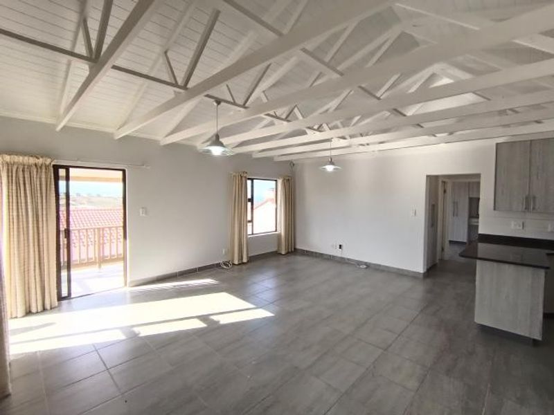 Spacious open-plan living area featuring high vaulted ceilings with exposed trusses, tiled flooring, and a modern kitchen with granite countertops.