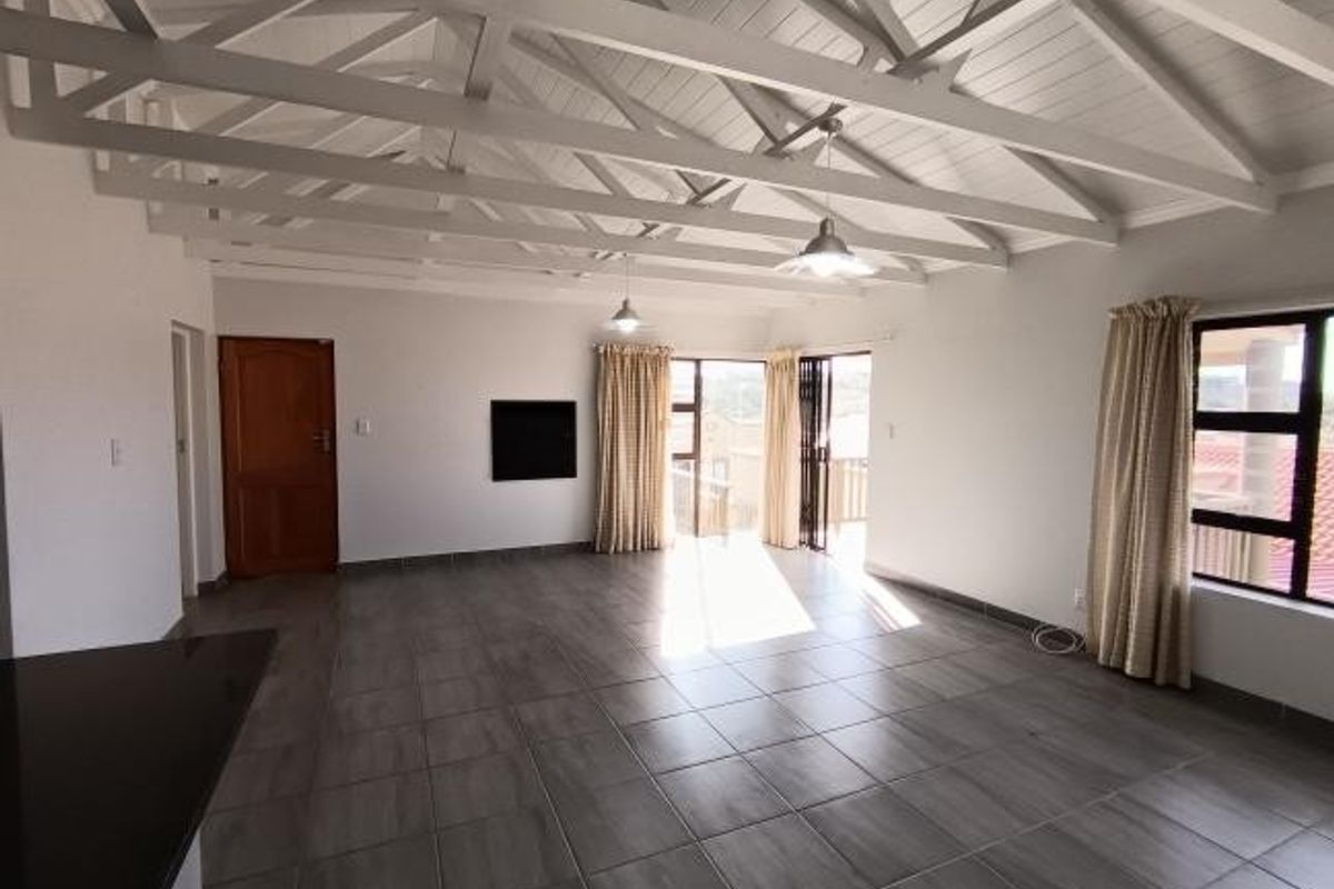 Spacious living area featuring a high vaulted ceiling with exposed white timber trusses, tiled flooring, and large sliding doors leading to an outdoor space.