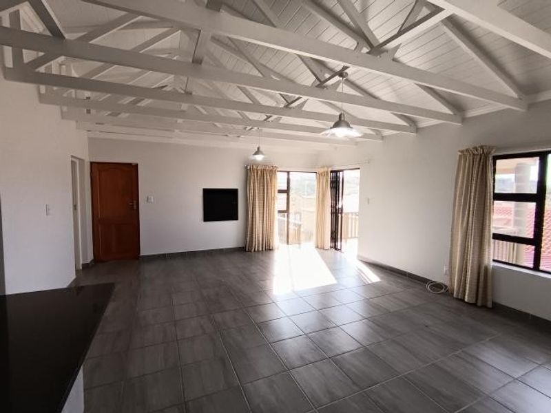 Spacious living area featuring a high vaulted ceiling with exposed white timber trusses, tiled flooring, and large sliding doors leading to an outdoor space.
