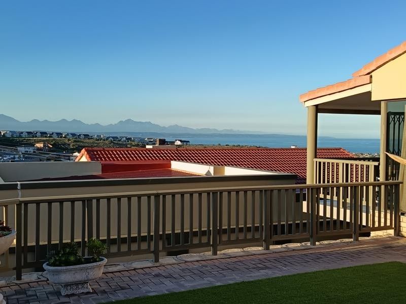 A covered patio area featuring paved flooring and railings, offering expansive views of the surrounding landscape and distant coastline.