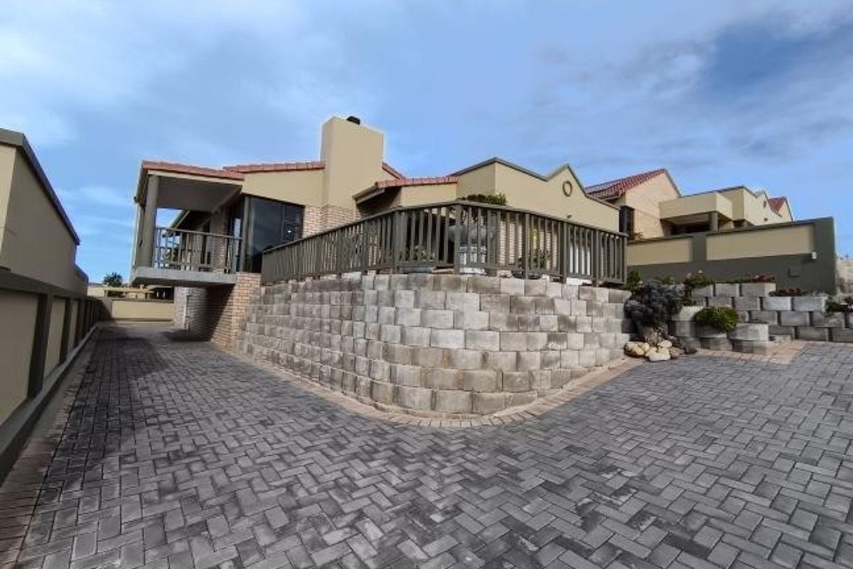 Rear exterior view of the house featuring a raised timber deck, retaining wall, and extensive paved driveway area.
