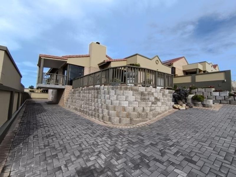 Rear exterior view of the house featuring a raised timber deck, retaining wall, and extensive paved driveway area.