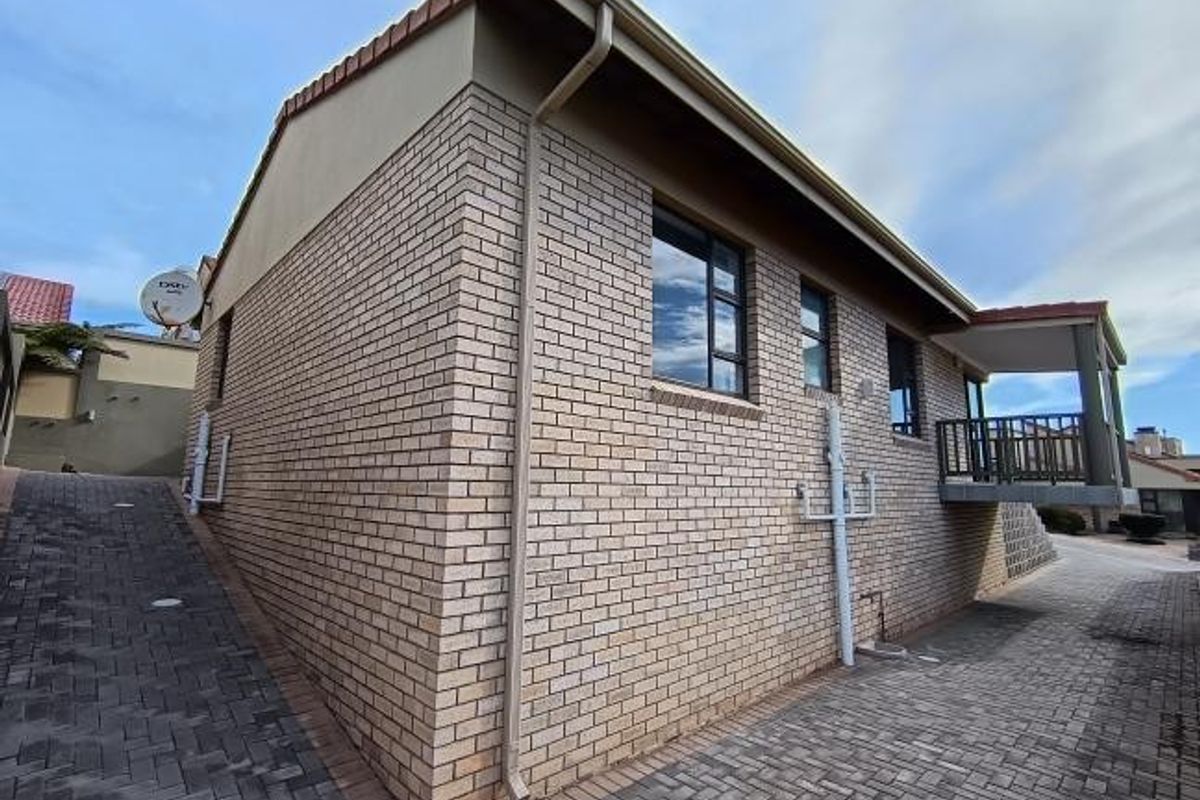 Side and rear view of a face brick house featuring a paved driveway, balcony, and tiled roof structure.
