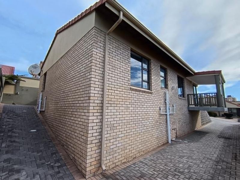 Side and rear view of a face brick house featuring a paved driveway, balcony, and tiled roof structure.