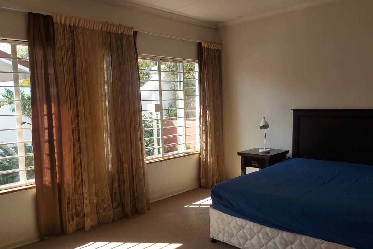 A bedroom featuring carpet flooring and large windows fitted with security bars, offering natural light and views of the exterior.