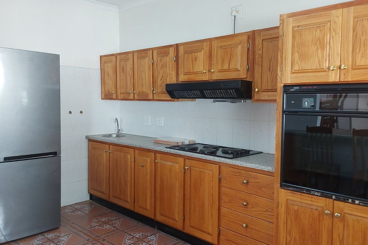 A functional kitchen featuring traditional wooden cabinetry, a built-in oven, hob, extractor fan, and tiled flooring with a neutral backsplash.