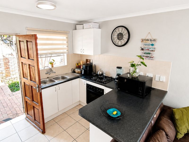 Compact open-plan kitchen featuring white cabinetry, dark countertops, gas hob, and tiled flooring, with direct access to the exterior patio area.