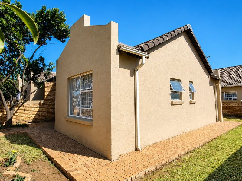 Rear view of the townhouse featuring a paved walkway, landscaped garden area, and brick boundary walls under a clear blue sky.