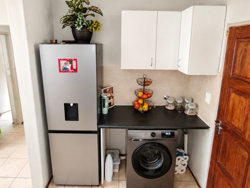 A functional laundry area featuring built-in upper cabinetry, a dark laminate countertop, tiled backsplash, and tiled flooring, adjacent to a timber door.