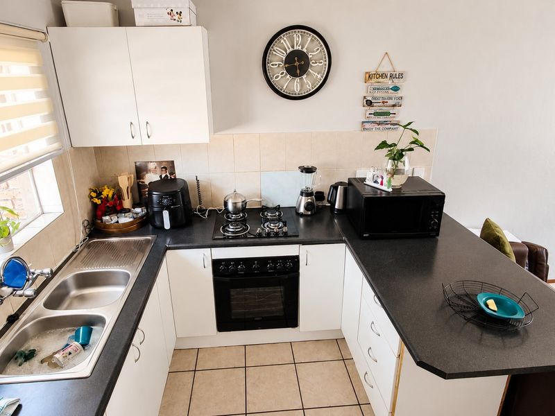A functional U-shaped kitchen featuring white cabinetry, dark laminate countertops, a gas hob, built-in oven, and a stainless steel double sink.