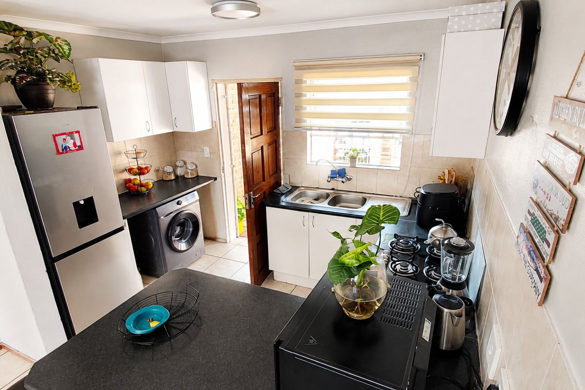 Compact kitchen featuring white cabinetry, dark laminate countertops, a gas hob, and integrated laundry plumbing, with direct access to an exterior door.