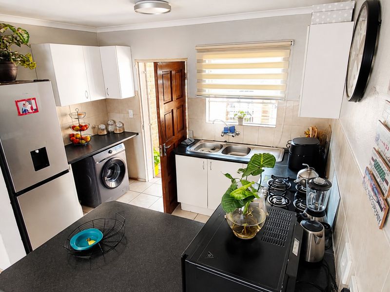 Compact kitchen featuring white cabinetry, dark laminate countertops, a gas hob, and integrated laundry plumbing, with direct access to an exterior door.