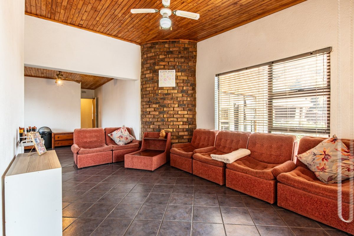 Spacious living room featuring a prominent exposed brick feature wall, timber ceiling, tiled flooring, and large windows with venetian blinds.
