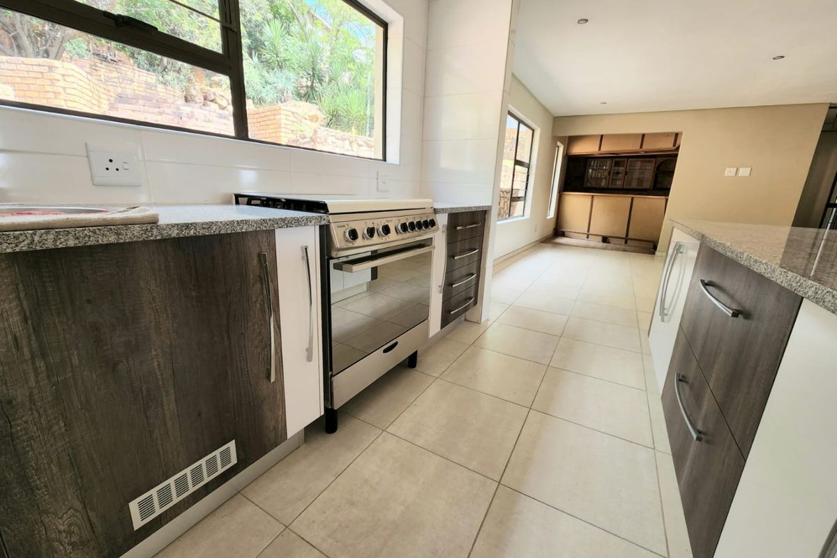 Modern kitchen featuring granite countertops, two-tone cabinetry, and a freestanding oven, with tiled flooring and large windows providing natural light.