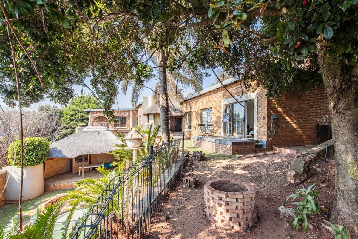 Rear exterior view featuring a brick house with sliding doors, a thatched lapa, and a rustic brick fire pit in a garden setting.