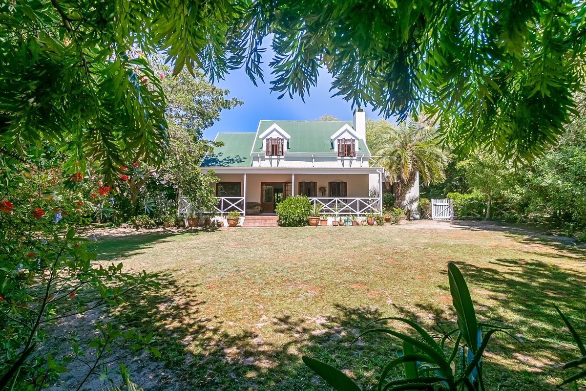 A charming cottage-style home featuring a green metal roof, dormer windows, and a spacious covered patio overlooking a large, established garden.