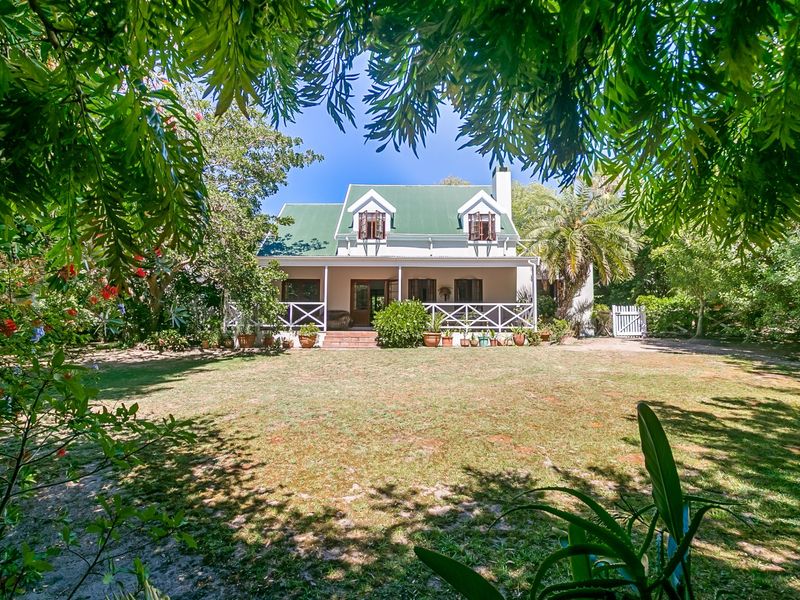 A charming cottage-style home featuring a green metal roof, dormer windows, and a spacious covered patio overlooking a large, established garden.