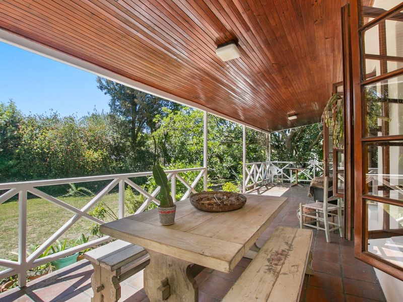 A spacious covered patio featuring a warm timber-clad ceiling, terracotta tiled flooring, and a classic cross-brace balustrade overlooking the garden.
