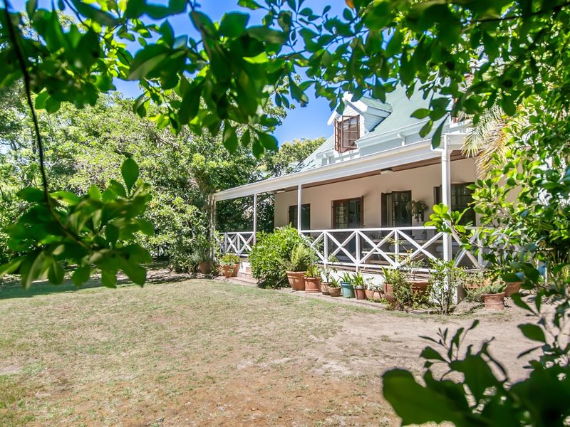 A charming rear view of the house featuring a spacious covered veranda with a classic timber balustrade, set within a lush garden.