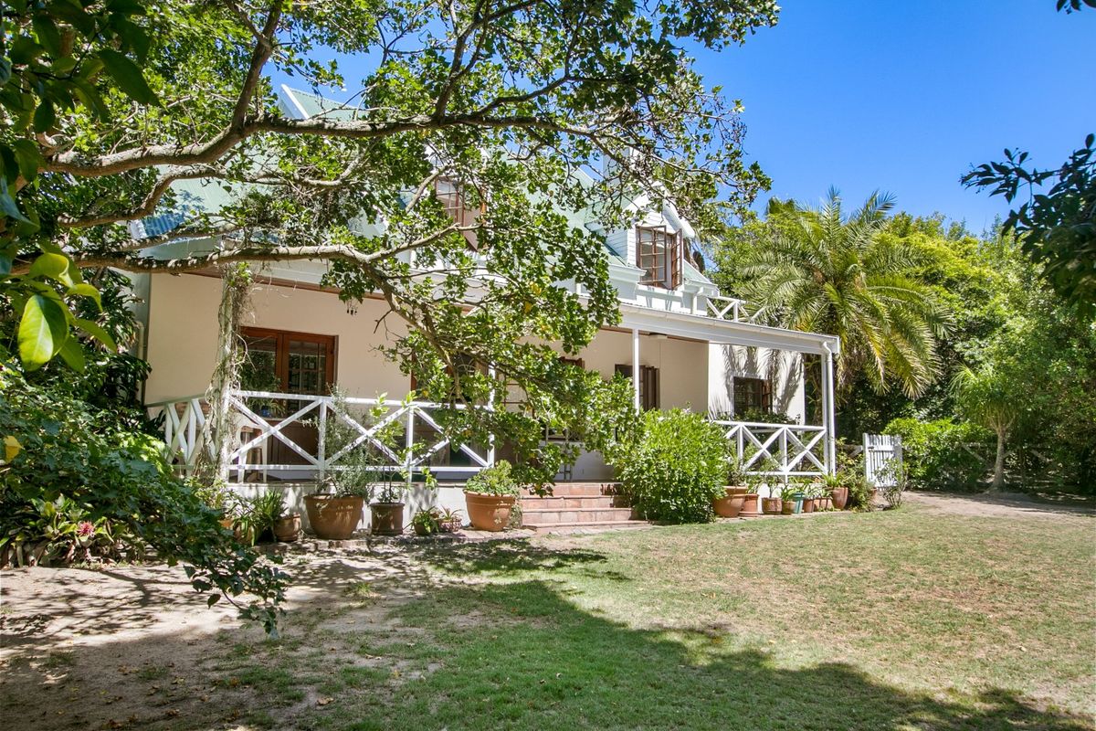A charming rear view of the house featuring a covered patio with timber balustrades, set within a lush, established garden.