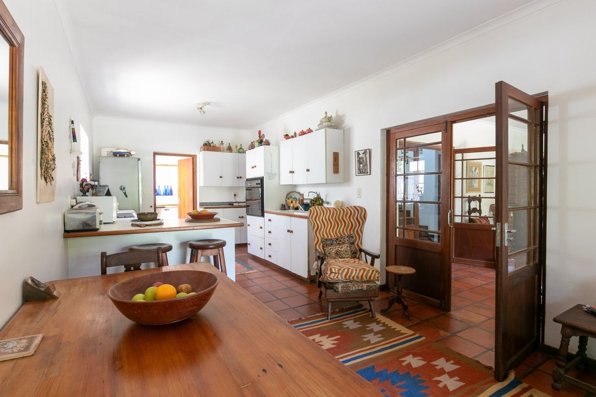 A functional kitchen featuring white cabinetry, a built-in oven, and traditional terracotta floor tiles, connected to adjacent living spaces via timber-framed glass doors.
