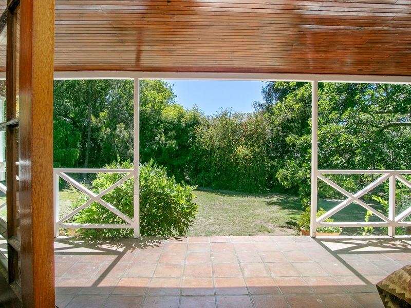 A covered patio featuring a timber-clad ceiling, tiled flooring, and a white timber balustrade, overlooking a lush green garden.