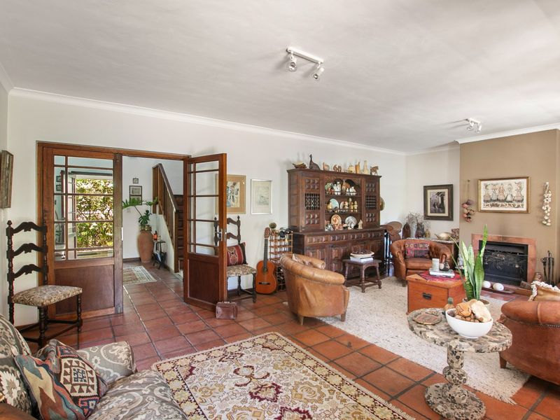Spacious living room featuring traditional terracotta floor tiles, a built-in fireplace, and timber-framed glass doors leading to the entrance hall.