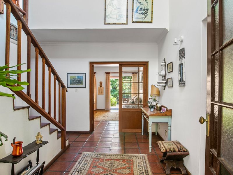 Welcoming entrance hall featuring terracotta floor tiles, a timber staircase, and a glass-paneled door leading through to the living area.