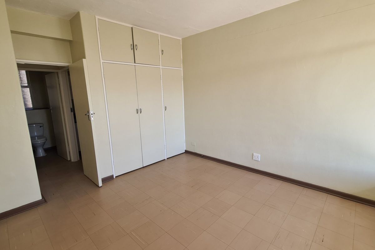 An empty bedroom featuring built-in cupboards and vinyl tile flooring, with an adjacent view into a bathroom area.