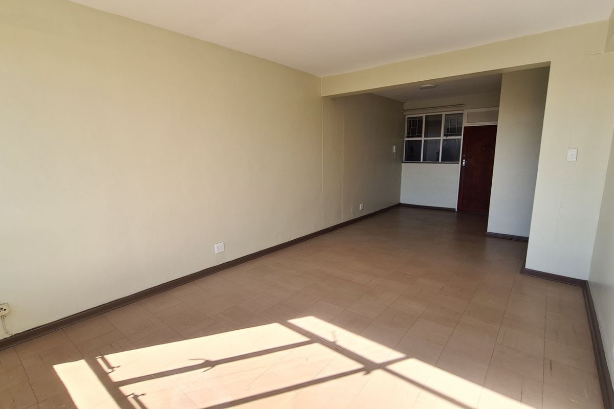 A spacious, empty living area featuring neutral wall tones and tiled flooring, providing a versatile blank canvas for commercial or office use.