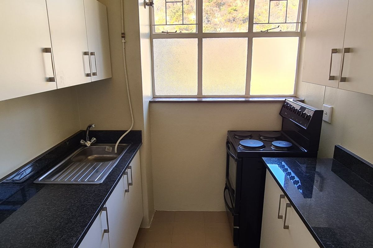 A compact kitchen featuring granite countertops, built-in cabinetry, and a stainless steel sink, with a window providing natural light.