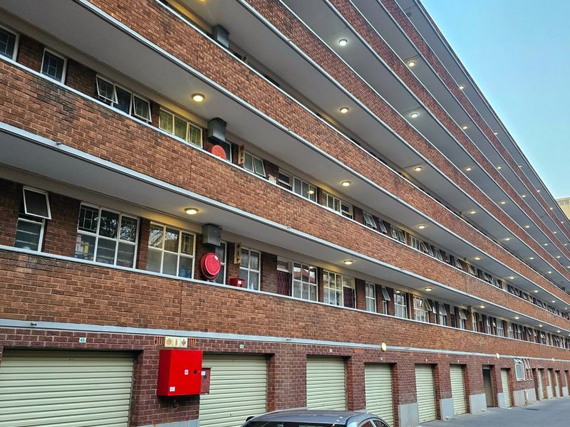 A multi-story commercial or residential building featuring a face brick facade, multiple ground-level garage units, and integrated fire safety equipment.