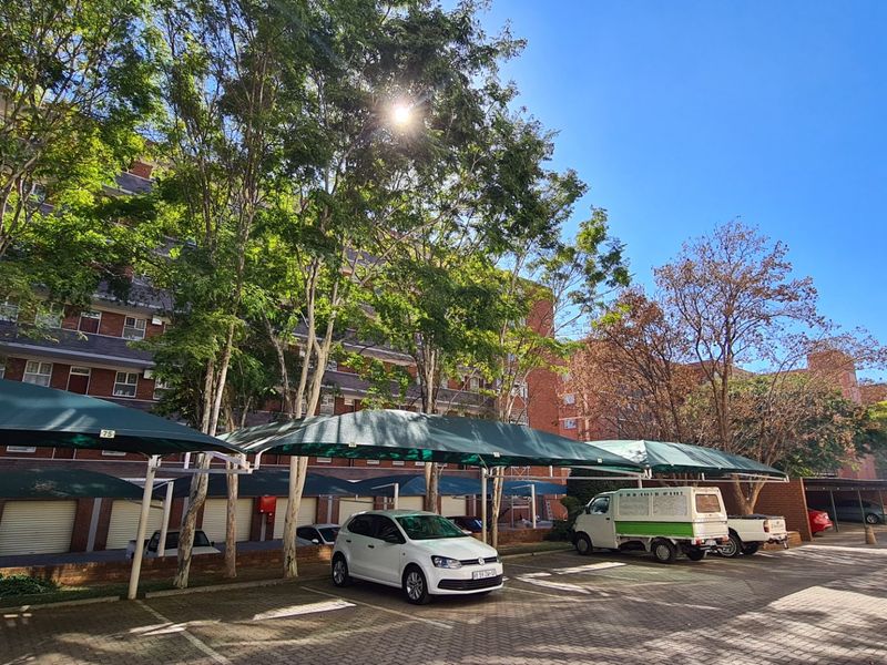 Exterior view of a commercial property featuring a paved parking area with shade cloth carports and brick building facade with roller shutter garage doors.