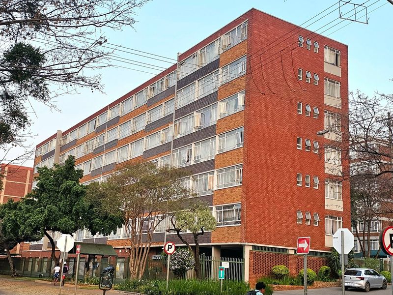 A multi-story commercial or residential brick building featuring a prominent facade, metal-framed windows, and established perimeter landscaping.
