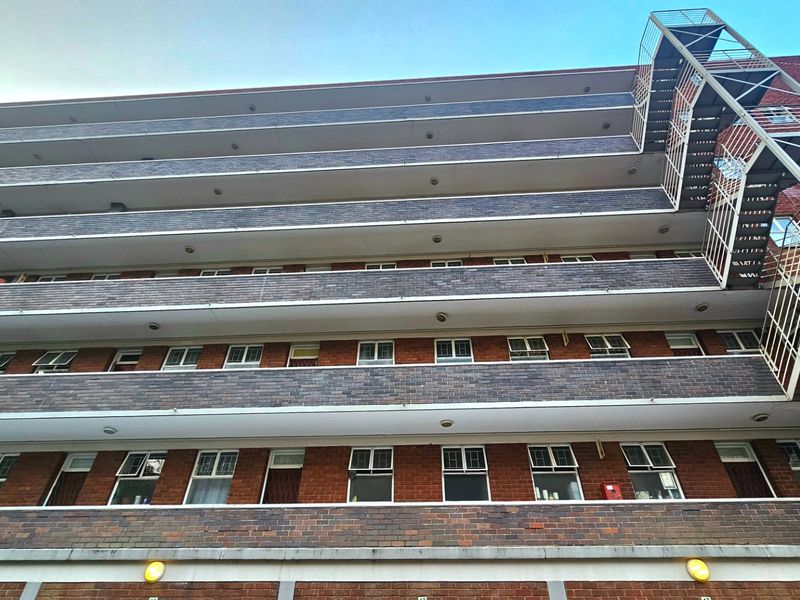 Low-angle view of a multi-story commercial brick building featuring external fire escape stairs and multiple levels of balconies.