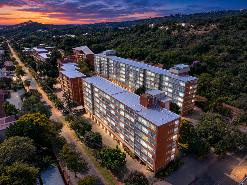 Aerial view of a large multi-story brick residential apartment complex situated in a suburban landscape at sunset.