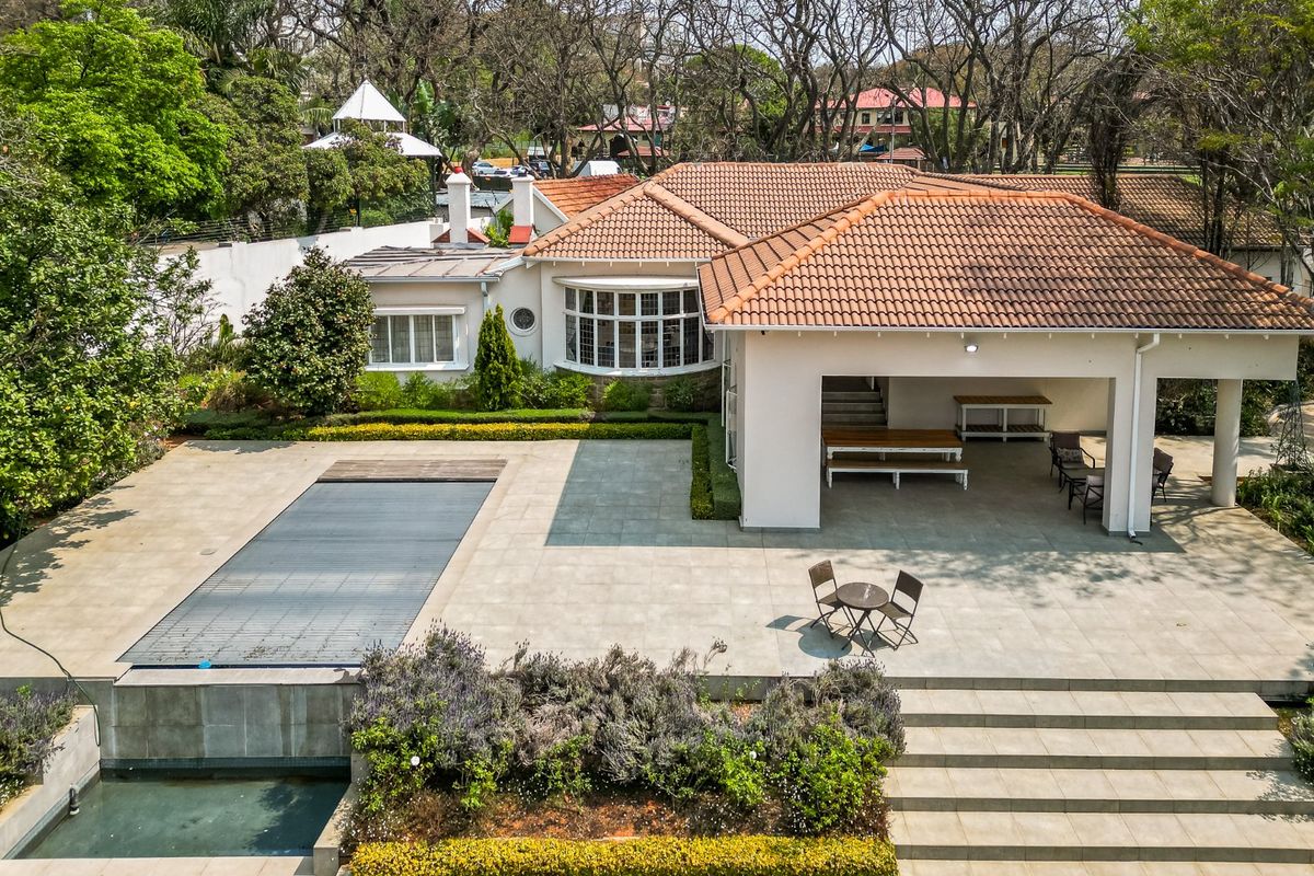 Aerial view of a well-maintained rear exterior featuring a spacious tiled patio, swimming pool with cover, and landscaped garden area.