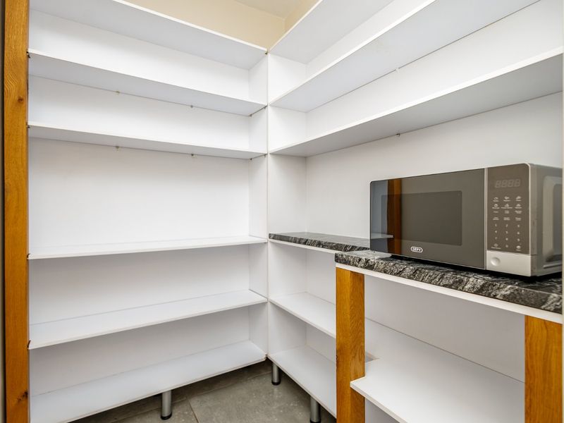 A clean and functional scullery or pantry area featuring extensive built-in white shelving and a granite countertop with a built-in microwave.