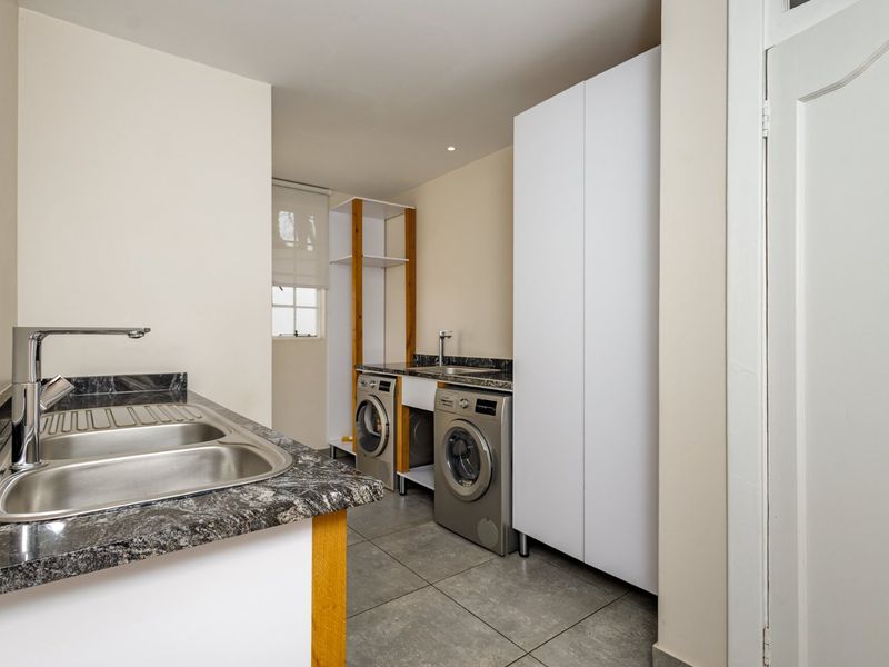 A functional laundry room featuring tiled flooring, granite countertops, and dual sink areas with built-in storage cabinetry.