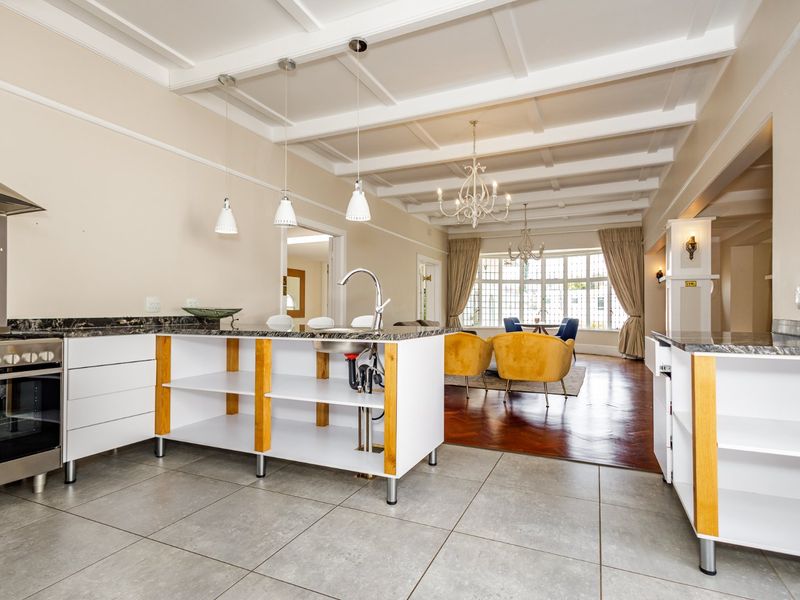 Open-plan kitchen and living area featuring a coffered ceiling, kitchen island with stone countertops, and a blend of tiled and hardwood flooring.