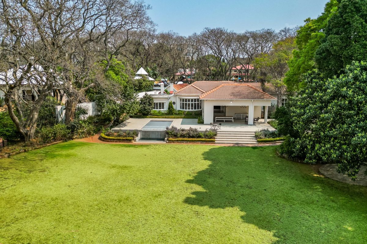 Aerial view of a spacious property featuring a large manicured lawn, a swimming pool, and a covered patio area.