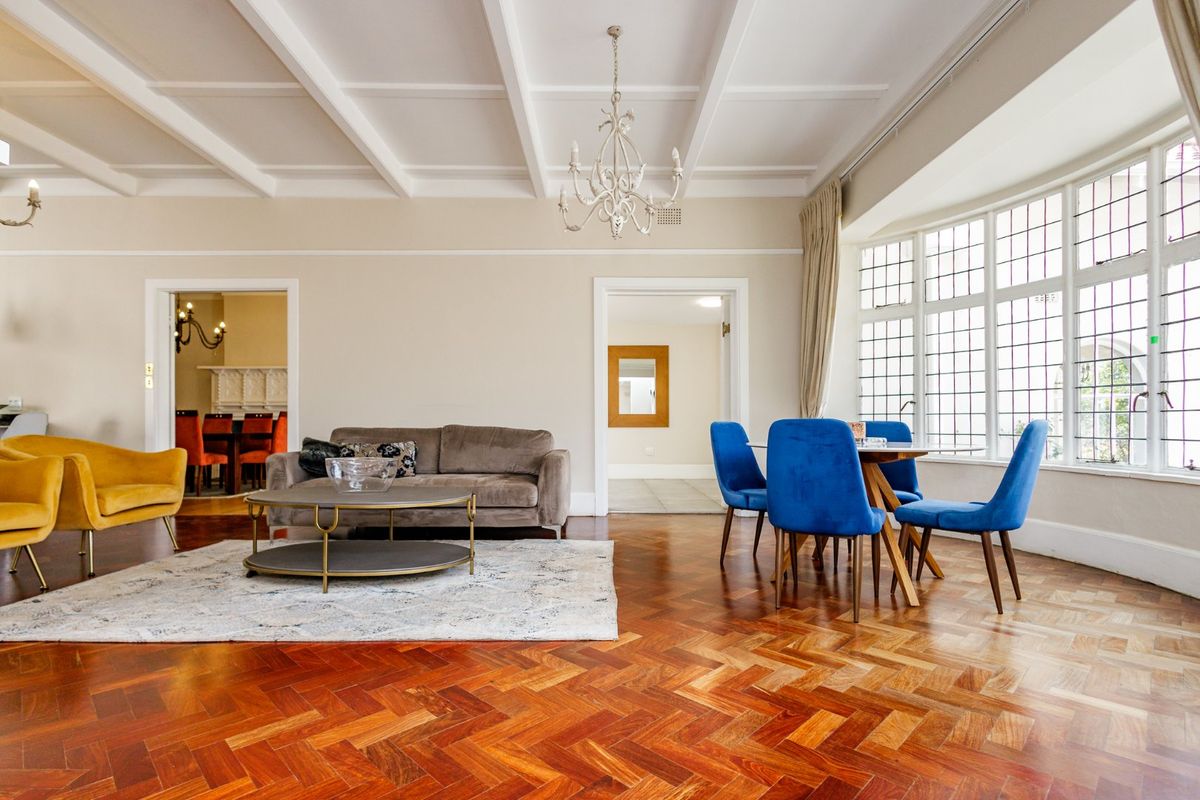 Spacious living room featuring elegant herringbone timber flooring, a classic coffered ceiling, and a large leaded glass bay window providing ample natural light.
