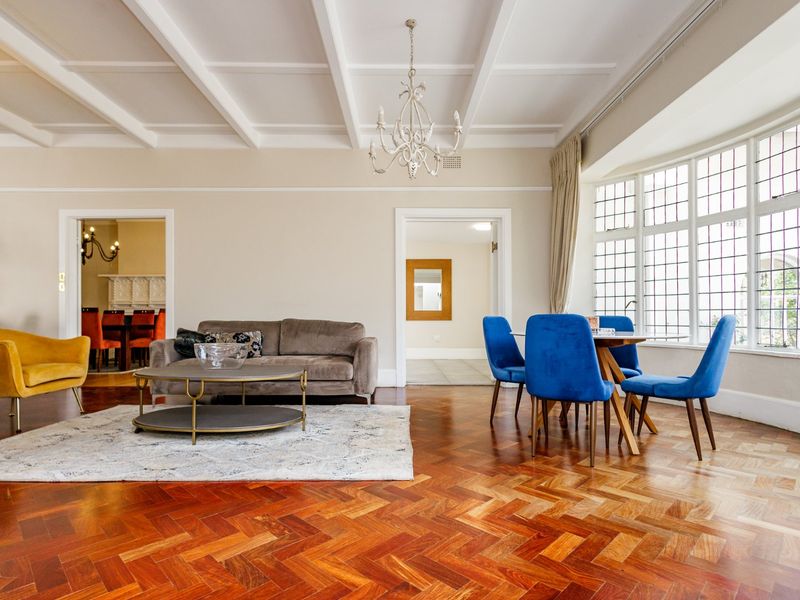 Spacious living room featuring elegant herringbone timber flooring, a classic coffered ceiling, and a large leaded glass bay window providing ample natural light.