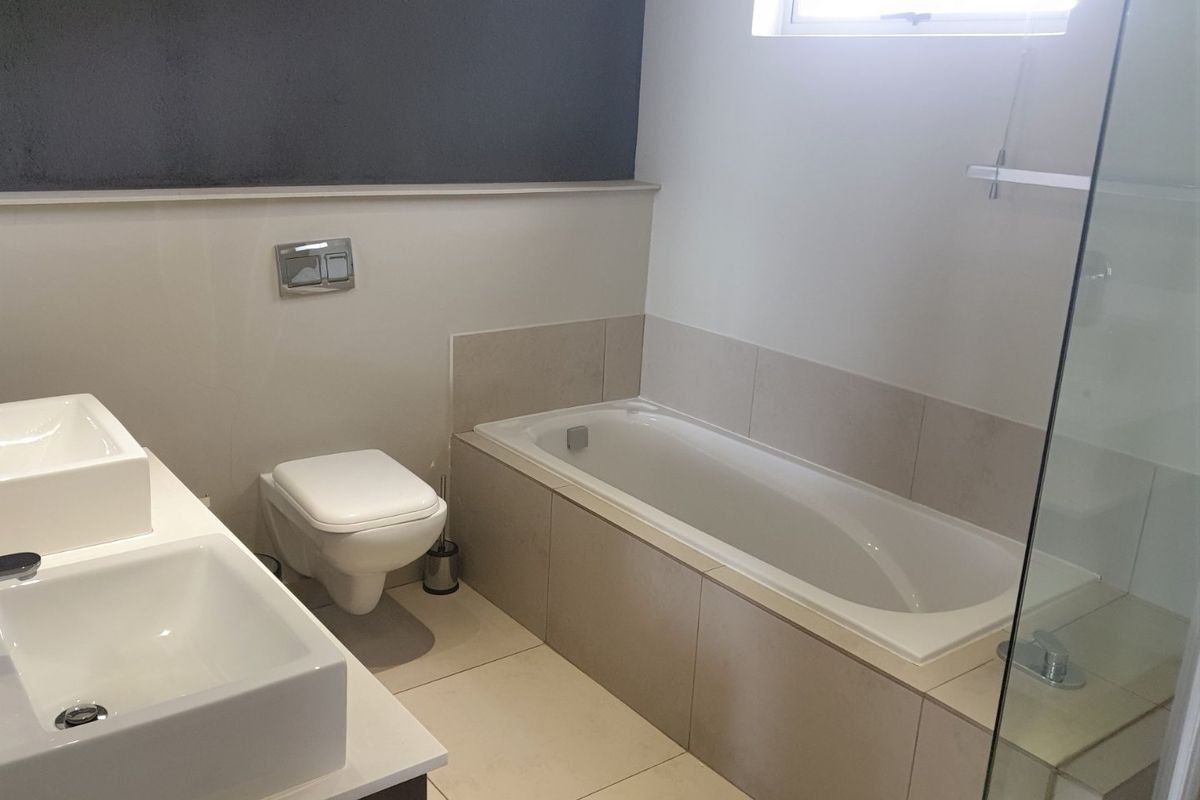 Modern bathroom featuring a double vanity, wall-hung toilet, and a built-in bathtub with neutral tiling and a glass shower enclosure.
