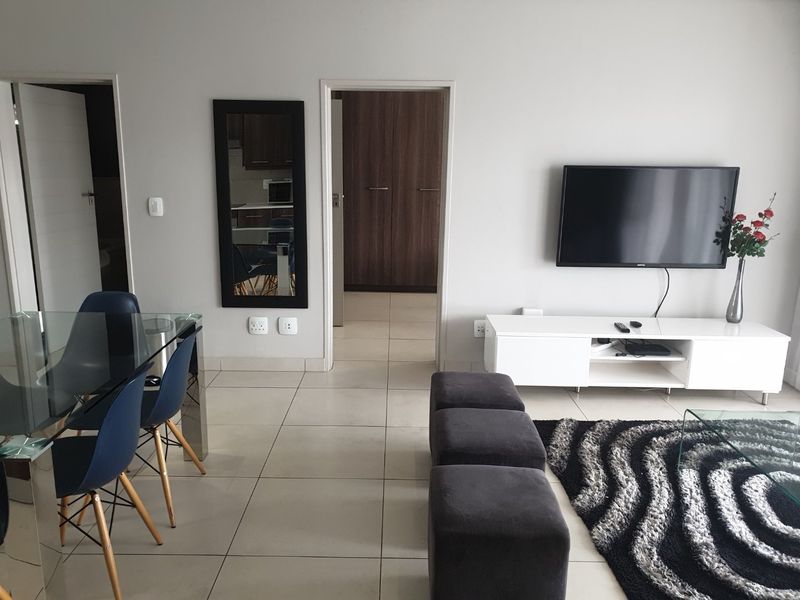 An open-plan living and dining area featuring neutral tiled flooring, clean wall finishes, and direct access to adjacent rooms with built-in storage.
