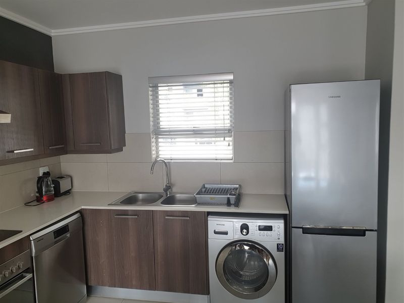 A functional kitchen featuring modern laminate cabinetry, stone countertops, a double sink, and integrated appliances including a dishwasher and washing machine.