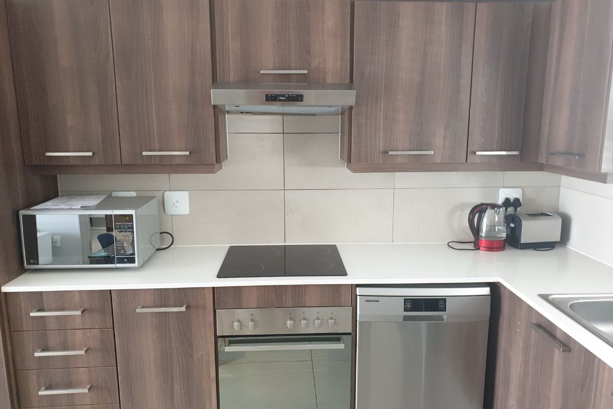 Modern kitchen featuring wood-grain cabinetry, stone countertops, tiled backsplash, and integrated stainless steel appliances including an oven, hob, and dishwasher.